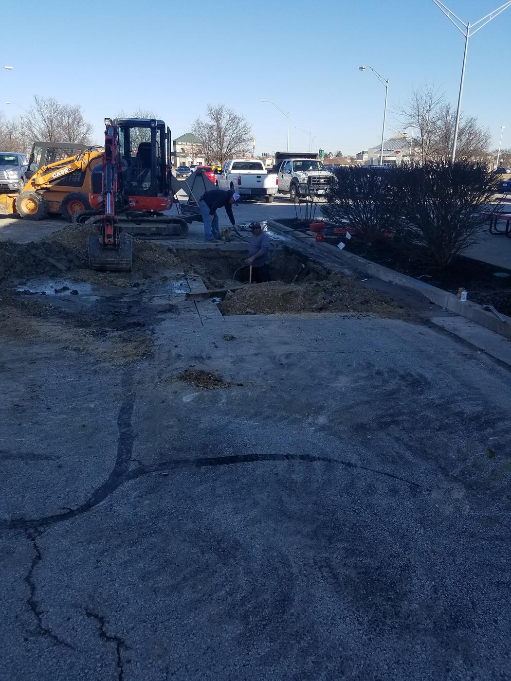 Underground work in a shopping center parking lot with a mini excavator, a skid steer and a dump truck